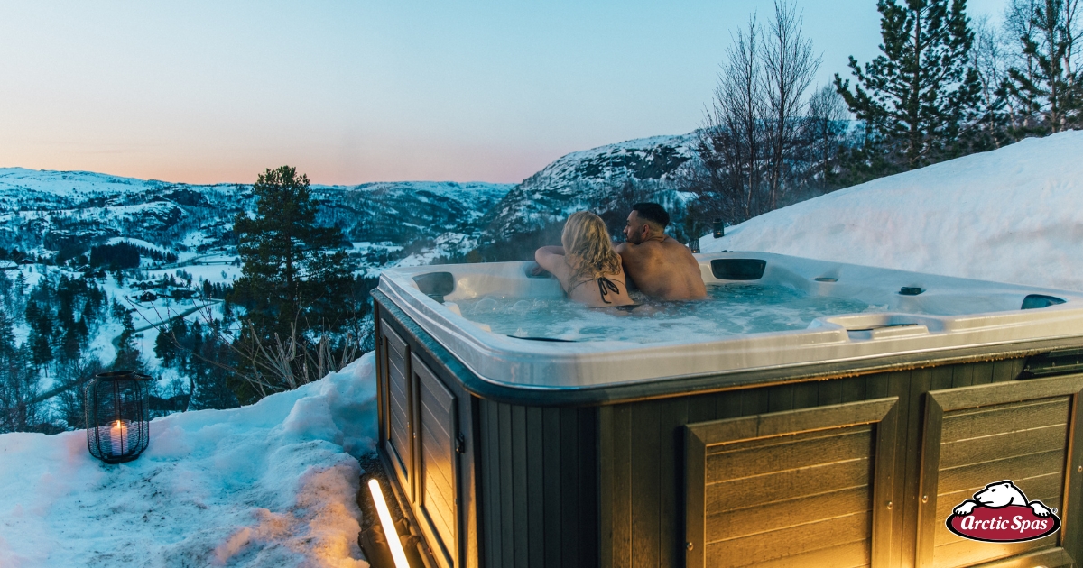 Couple relaxing in an Arctic Spas hot tub overlooking snowy mountains at dusk